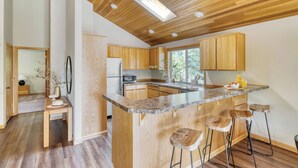A modern kitchen with wooden cabinets, a granite countertop, and a central island with bar stools. - Tanner by Avantstay Modern Cascades Escape (Bend)