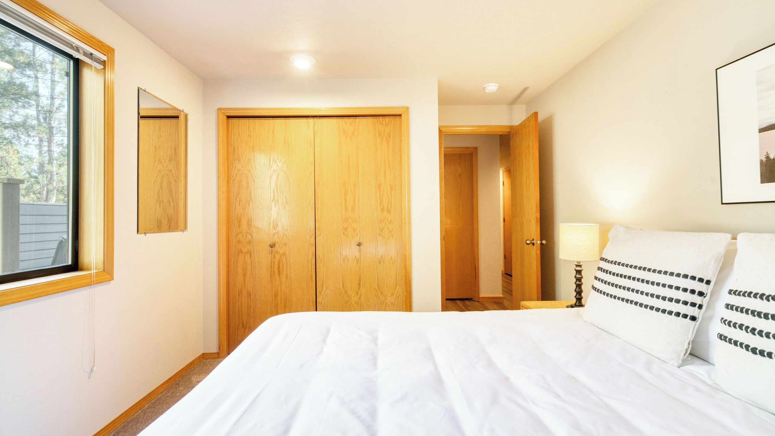 A bedroom with a large bed, wooden wardrobe, a bedside table with a lamp, and a framed picture on the wall.