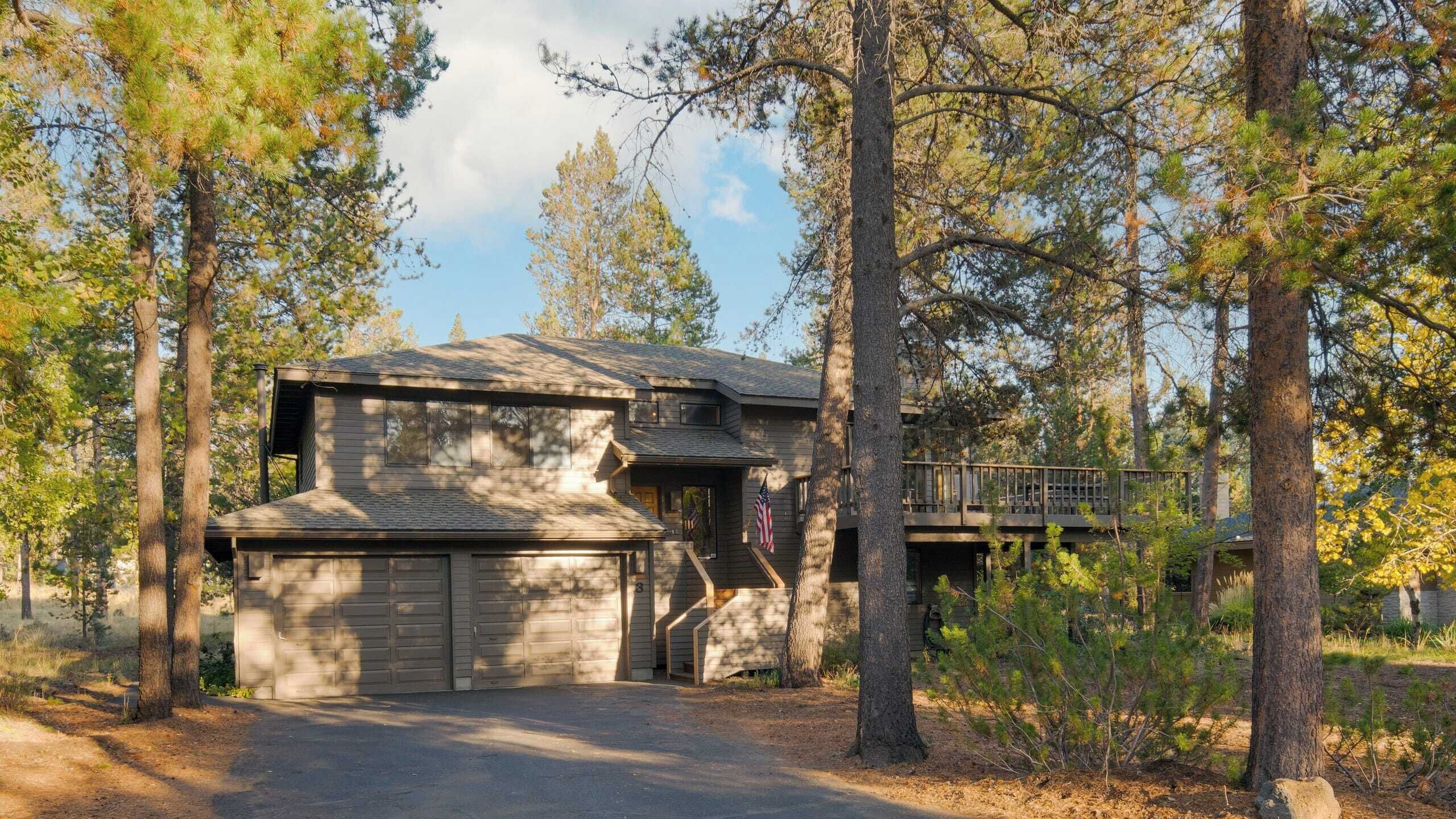 A two-story cabin with a garage, surrounded by tall pine trees.