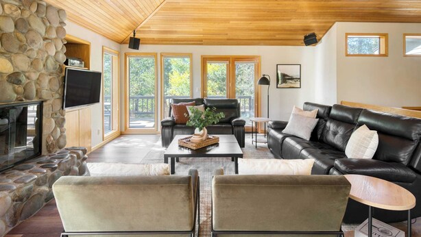 A spacious living room with a stone wall, a fireplace, a leather sofa, and a coffee table. - Tanner by Avantstay Modern Cascades Escape (Bend)