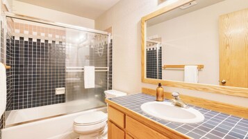 Ein Badezimmer mit Duschkabine aus Glas, Toilette in Weiß, Waschbecken mit Holzschrank und einem großen Spiegel.