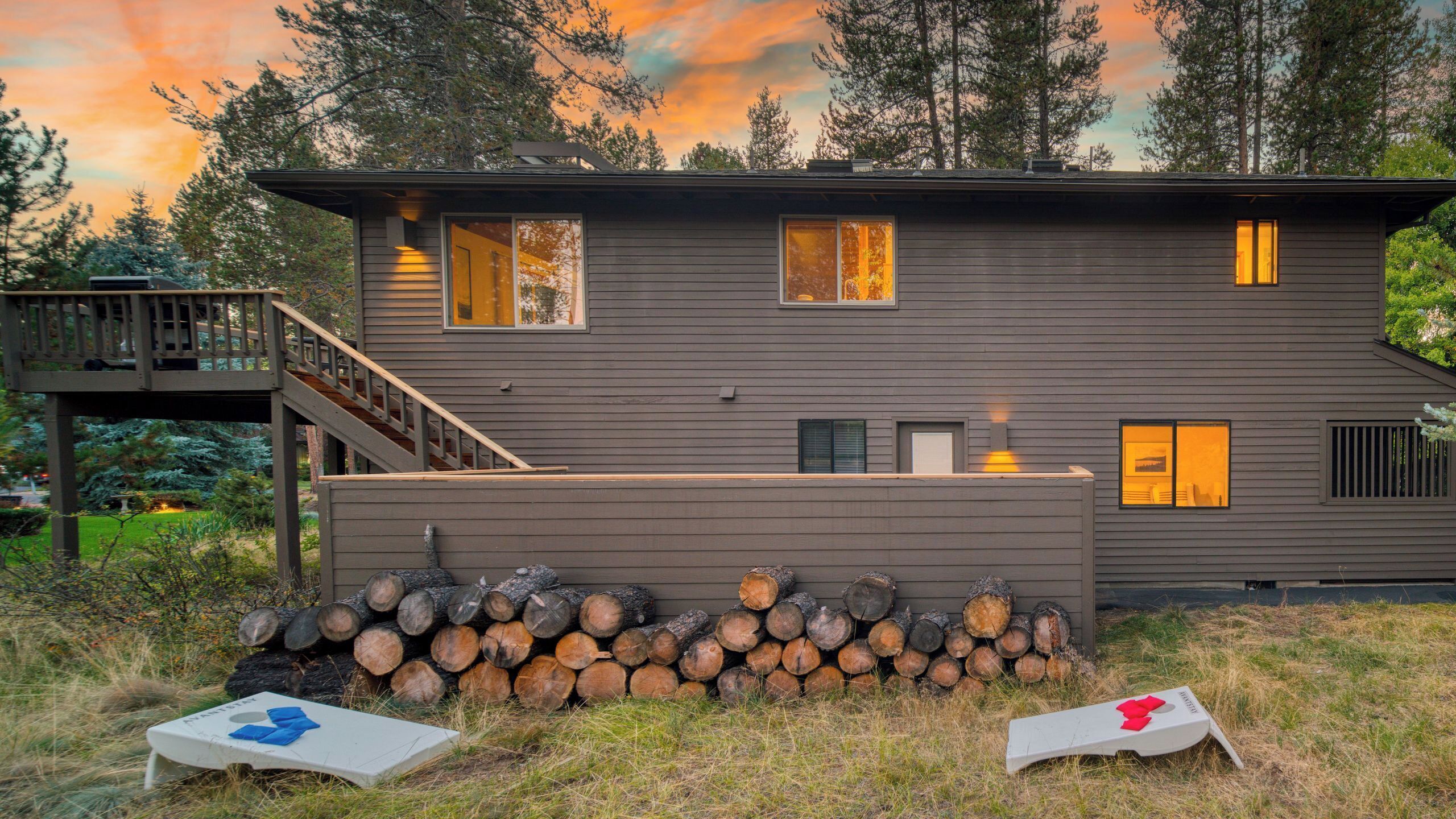 Une maison moderne à deux étages, dotée d’une terrasse, d’une cheminée et d’une pile de bois de chauffage.