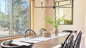 A dining area with a wooden table, chairs, a vase with greenery, and a painting on the wall. - Tanner by Avantstay Modern Cascades Escape (Bend)