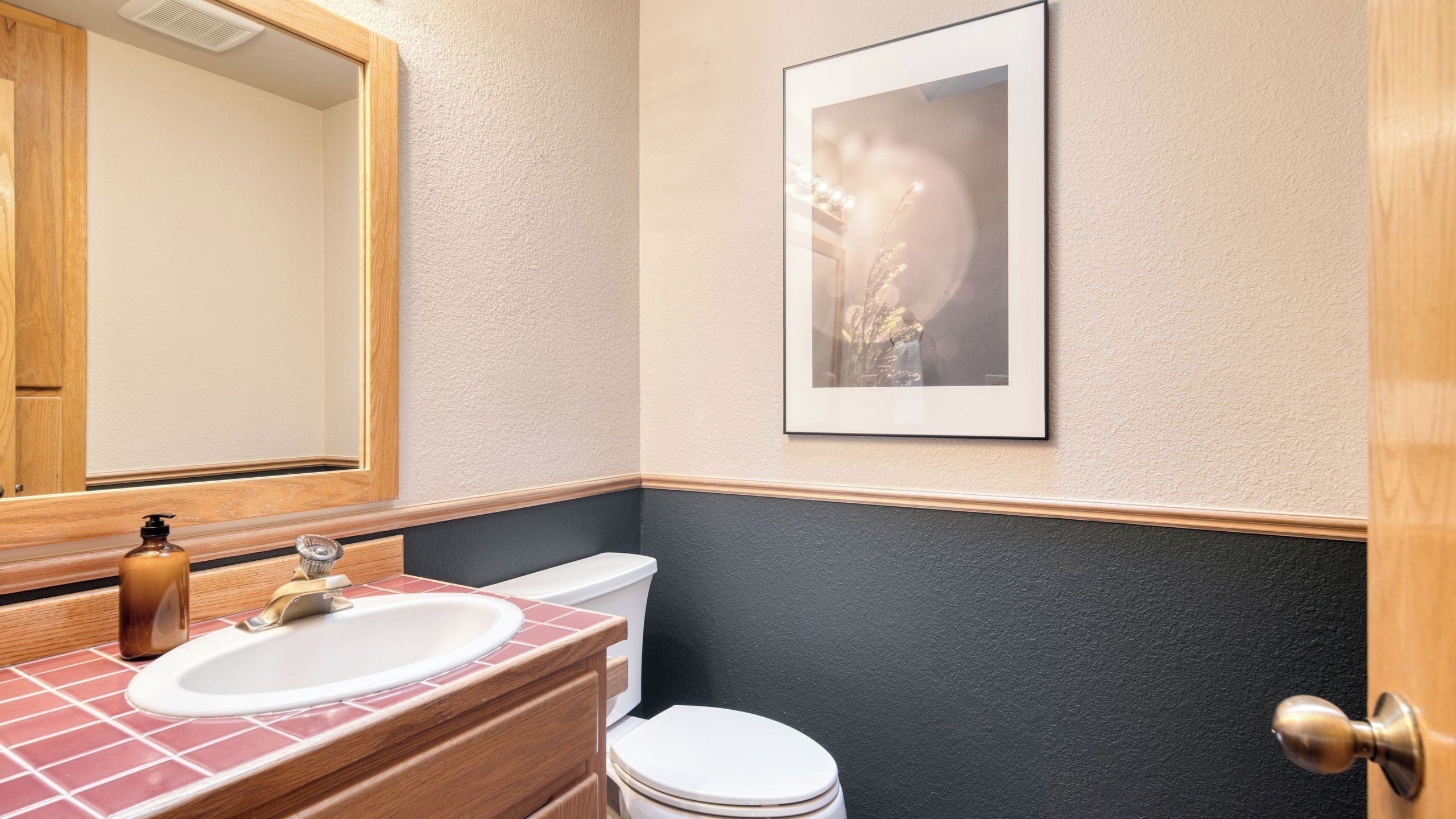 A bathroom with a wooden vanity, a sink, a toilet, and a framed picture on the wall.