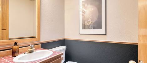 A bathroom with a wooden vanity, a sink, a toilet, and a framed picture on the wall.