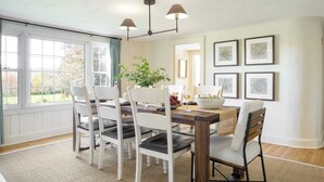Un espace repas avec une table en bois, des chaises blanches et un luminaire suspendu.