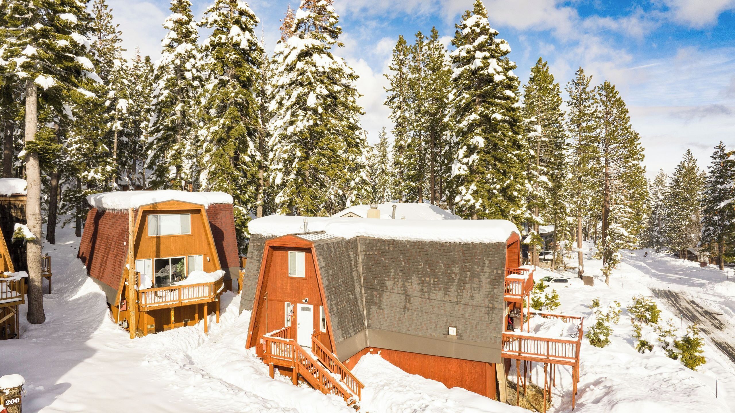 Una cabaña nevada con cabañas de madera, una terraza de madera y un techo cubierto de nieve.