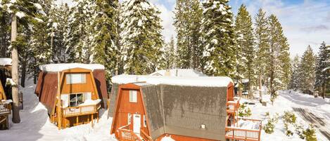 Una cabaña nevada con cabañas de madera, una terraza de madera y un techo cubierto de nieve.