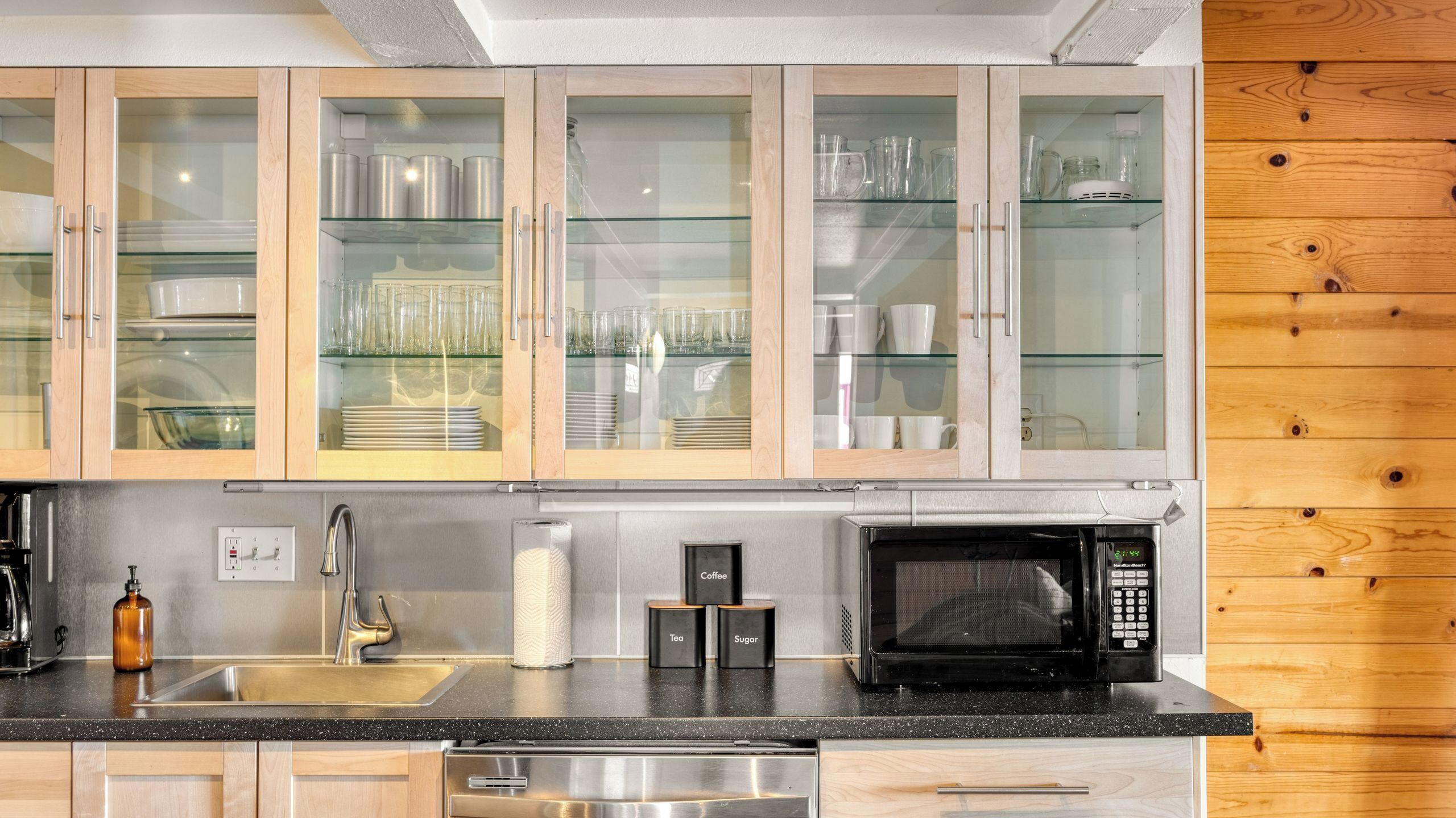 A kitchen with wooden cabinets, a stainless steel sink, a coffee machine, and a microwave.
