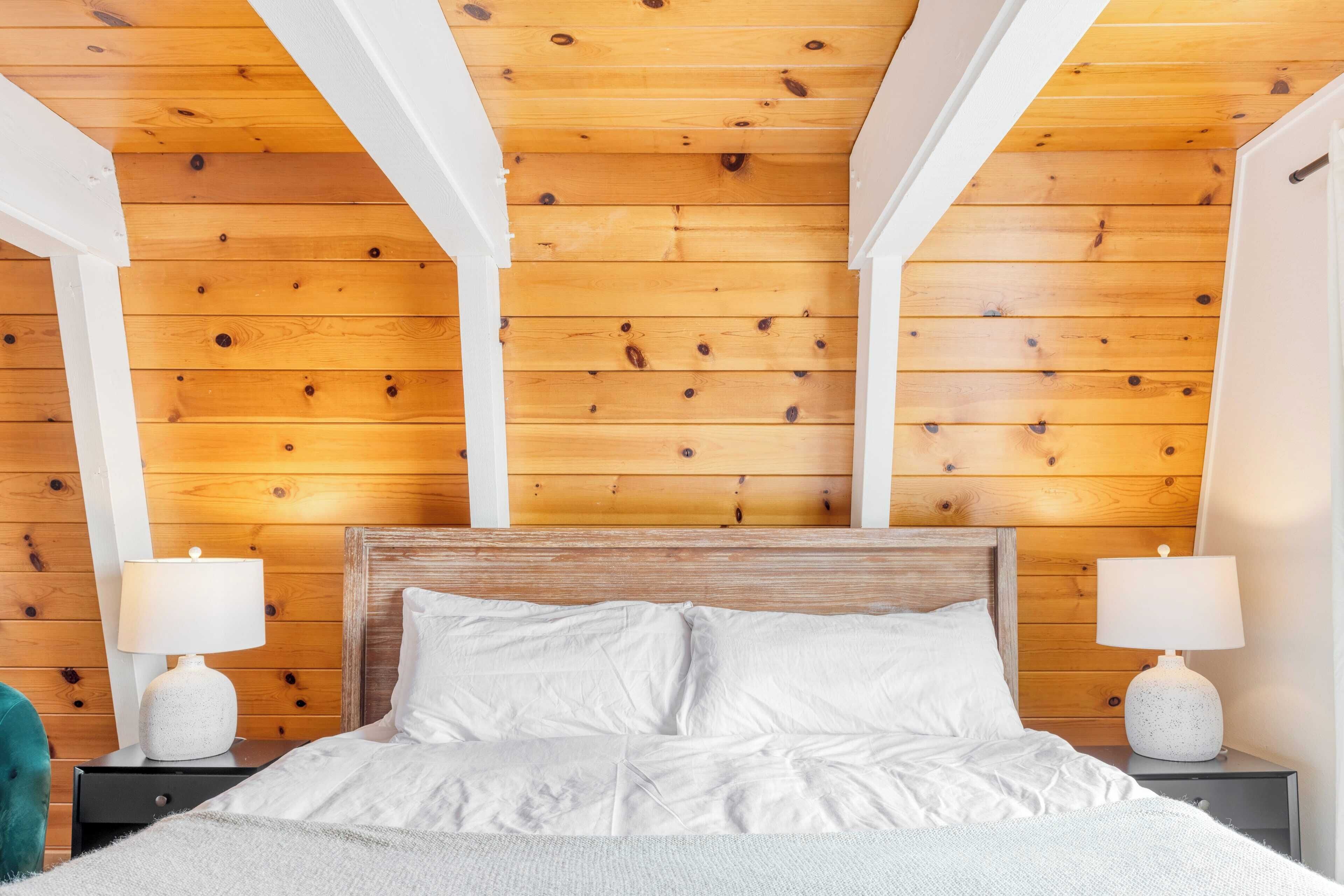 A bedroom with a wooden ceiling, white bedding, and two bedside lamps.