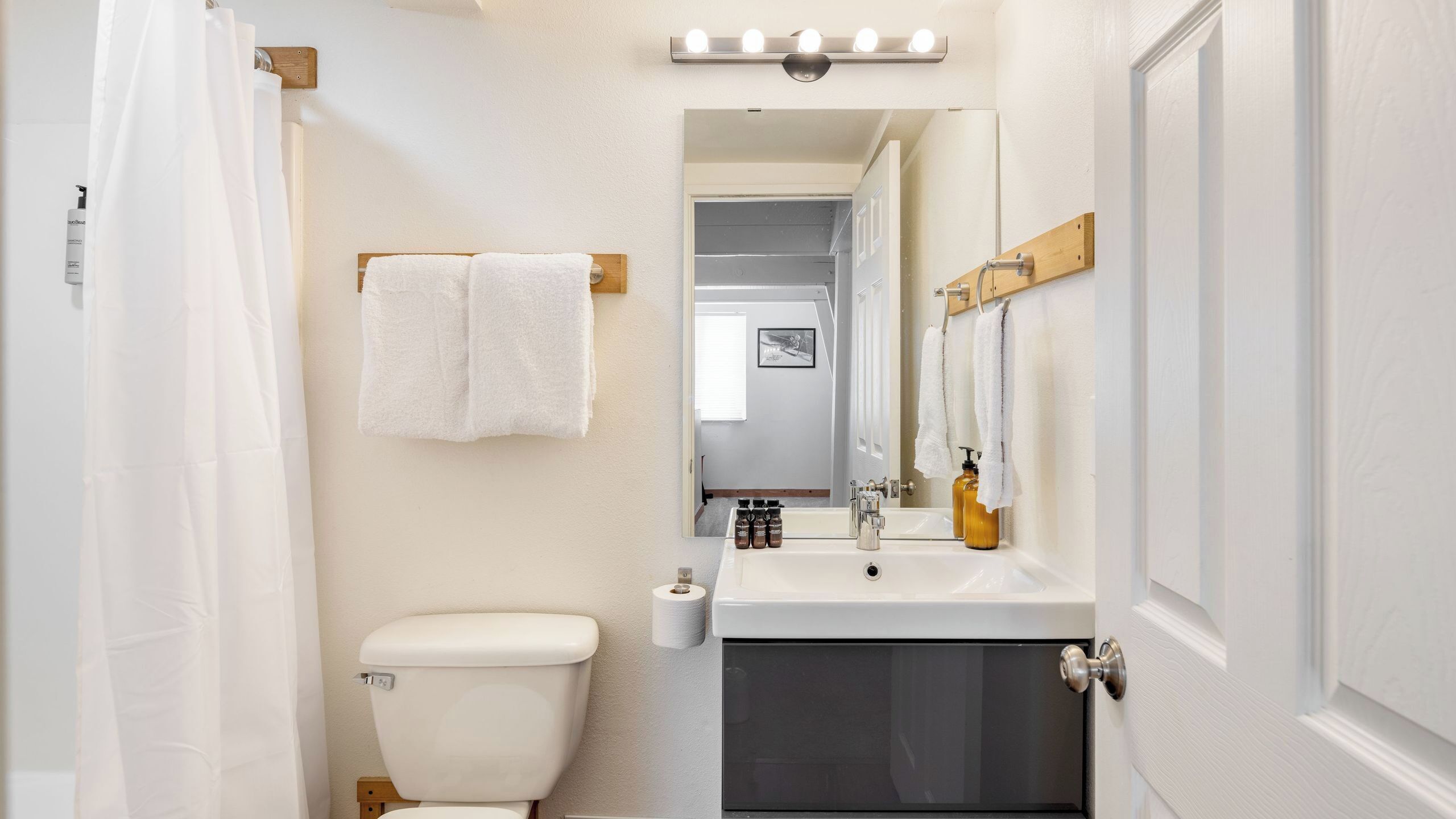 A bathroom with a toilet, sink, and mirror. There are towels hanging on the wall and a shower curtain.