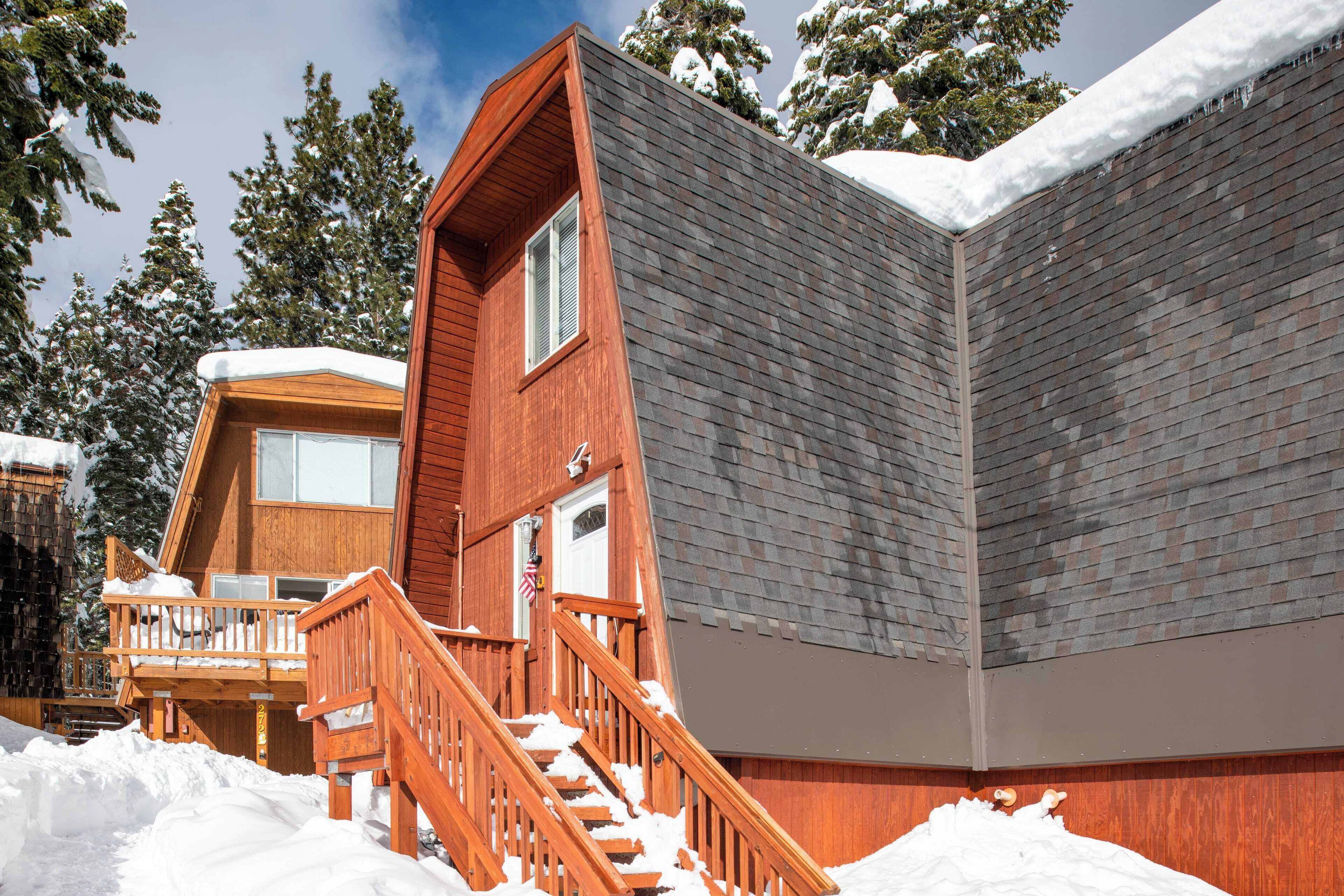A wooden cabin with a balcony and a staircase, surrounded by snow-covered trees.