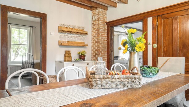 A dining area with a wooden table, white chairs, a brick column, a vase with sunflowers, and a basket with bread and tomatoes. - Cordelia by Avantstay Amazing Backyard, 10mins From Stockbridge! (Lee)