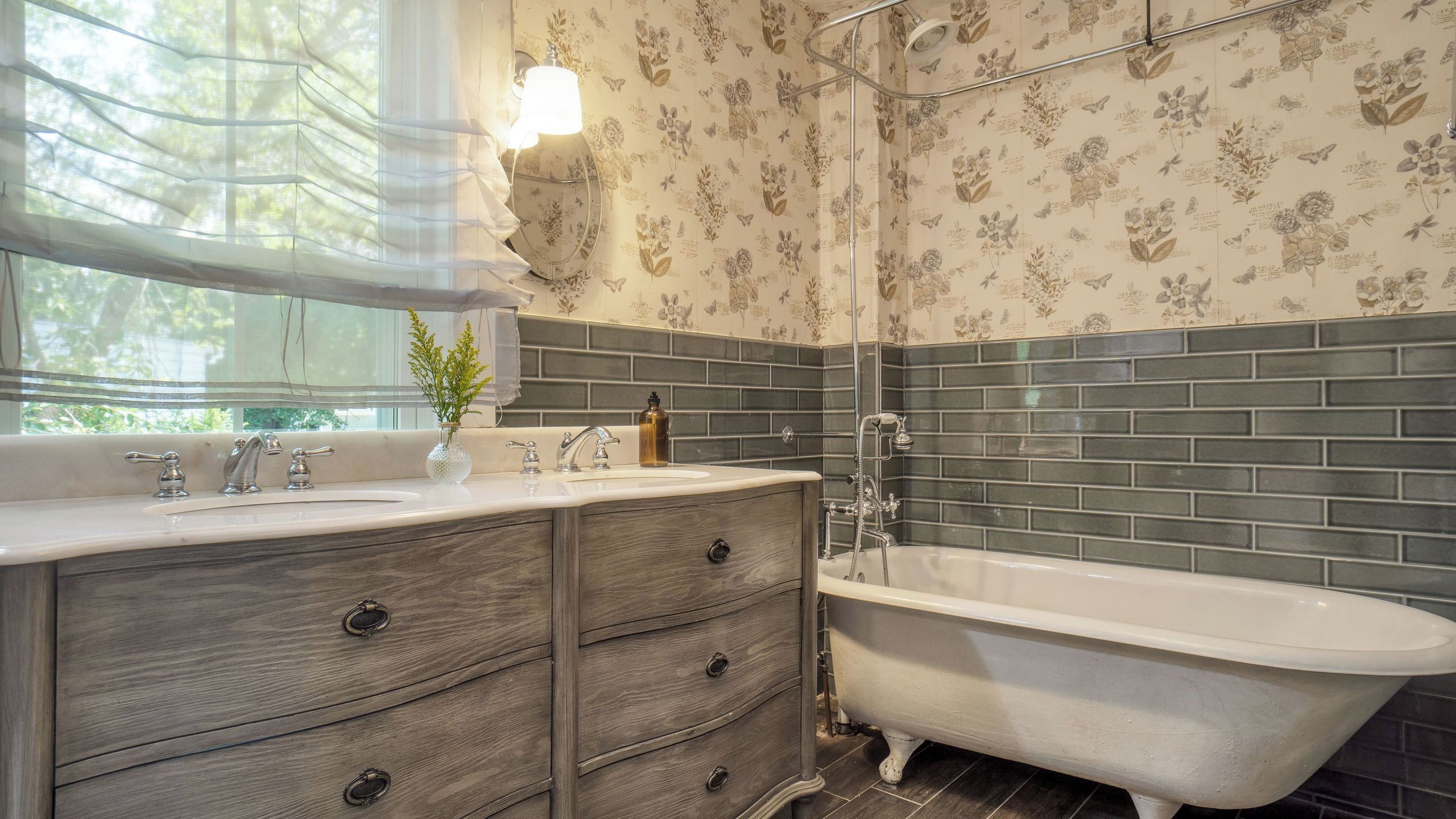 A bathroom with a freestanding bathtub, a vanity with a mirror, and a window with sheer curtains.