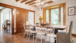 A dining area with a wooden table, white chairs, a chandelier, and a view through large windows. - Cordelia by Avantstay Amazing Backyard, 10mins From Stockbridge! (Lee)