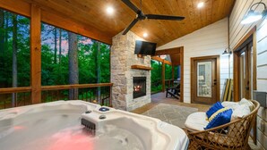 Un jacuzzi con chimenea de piedra, techo de madera y vistas a árboles.