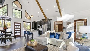 Un salón espacioso con un sofá grande, una zona de comedor con mesa y sillas, una cocina y vistas al exterior a través de amplias ventanas.
