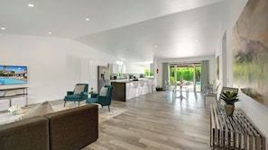 A spacious living area with a sofa, teal chairs, a TV, and a kitchen in the background. - Catalina by Avantstay Fully Remodeled Palm Springs Haven + Pool Permit#3432 (Palm Springs)