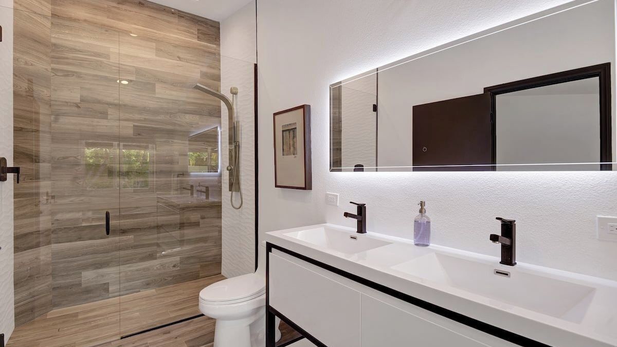 Ein modernes Badezimmer mit Duschkabine aus Glas, einem weißen Waschbecken mit großem Spiegel und einer weißen Toilette.