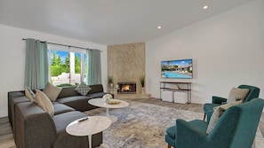 A modern living room with a sofa, two coffee tables, a fireplace, a TV, and a view of a pool. - Catalina by Avantstay Fully Remodeled Palm Springs Haven + Pool Permit#3432 (Palm Springs)