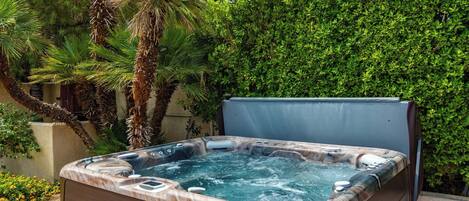 A hot tub with a marble exterior, surrounded by lush greenery and a palm tree.