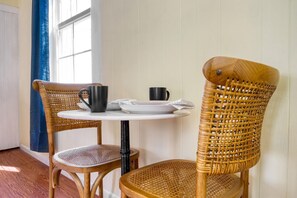 A dining area with wicker chairs and a round table, featuring a white plate, a black mug, and a white napkin. - Eloise by Avantstay Historic Upstate Apartment Near Hudson River (Saugerties)