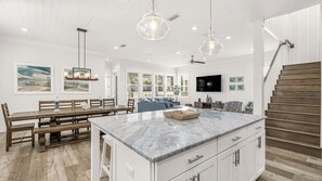 Una cocina amplia con una isla de mármol, mesa de comedor de madera e iluminación colgante.