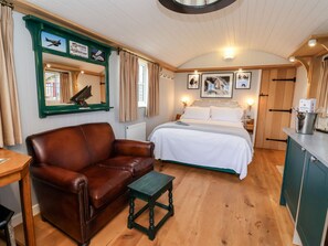 A cozy room with a bed, a leather couch, a small table, and a green-framed mirror. - Amy Johnson (York)