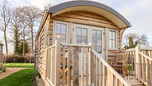 Una baita di legno con tetto curvo, un patio in legno e una scala che conduce all'ingresso.