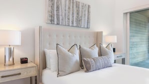 Une chambre d’hôtel avec un grand lit, deux tables de chevet, une œuvre d’art accrochée au mur et une fenêtre avec des stores.