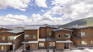 A modern wooden building with multiple units, large windows, and a view of mountains.
