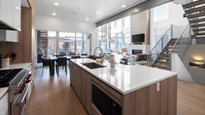 A modern kitchen with a central island, stainless steel appliances, and a dining area with a large window. - Slopewatch by Avantstay Ski-in/out Luxe Retreat (Park City)