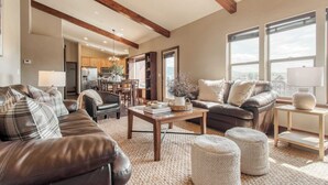 A spacious living room with a dark brown leather sofa, a wooden coffee table, and a large window providing a view of the city. - Lucky Bill by Avantstay Lake Views, 15mins to Park City Mtn (Heber City)