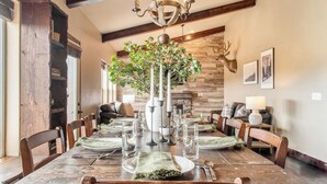 A dining room with a wooden table set for six, surrounded by chairs, a chandelier, and a large plant centerpiece. - Lucky Bill by Avantstay Lake Views, 15mins to Park City Mtn (Heber City)