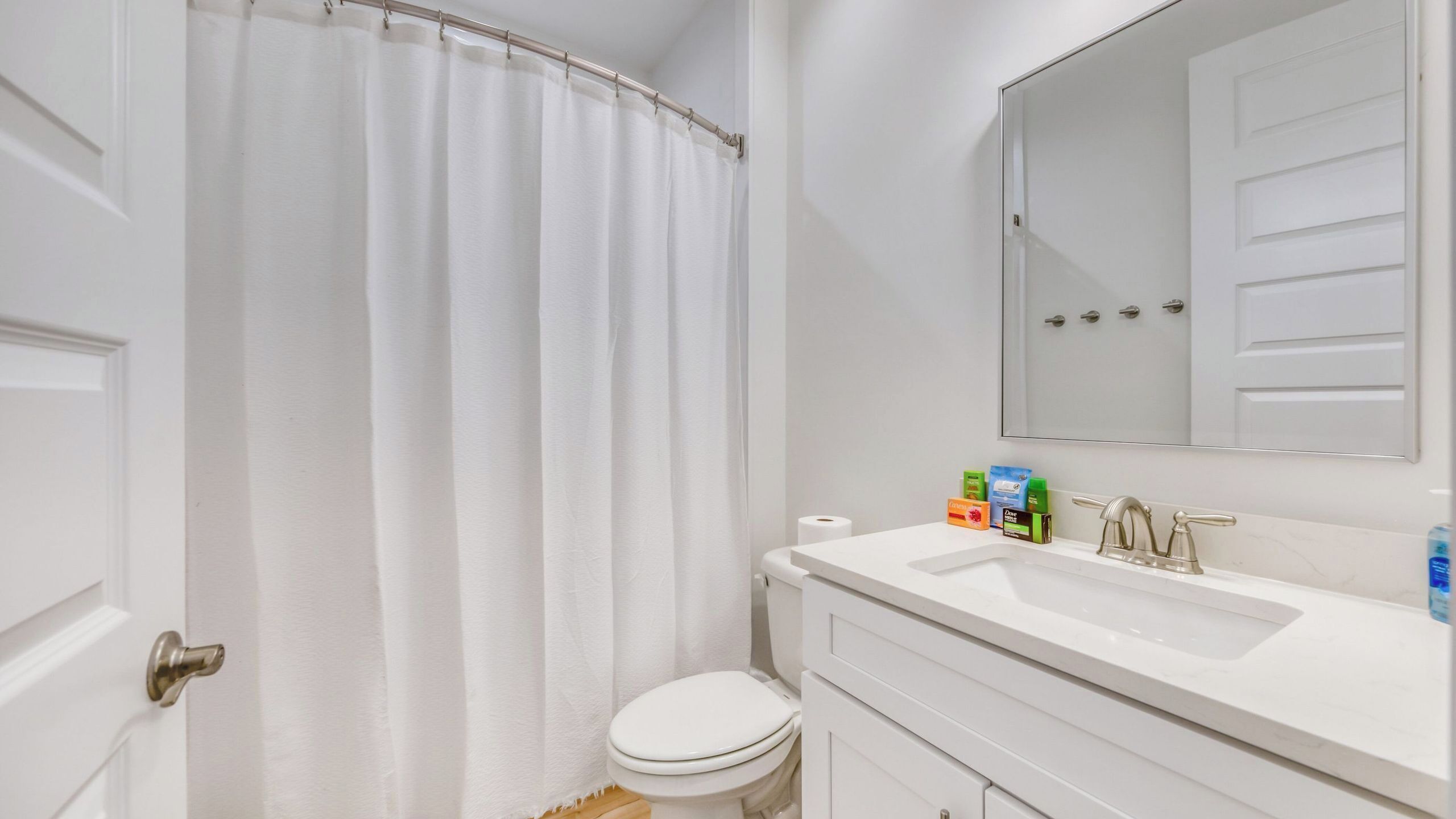Une salle de bain avec des toilettes blanches, un lavabo avec un miroir au-dessus et un rideau de douche.