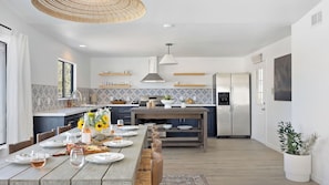 A modern kitchen with a dining area, featuring a large island, pendant lighting, and a built-in refrigerator.