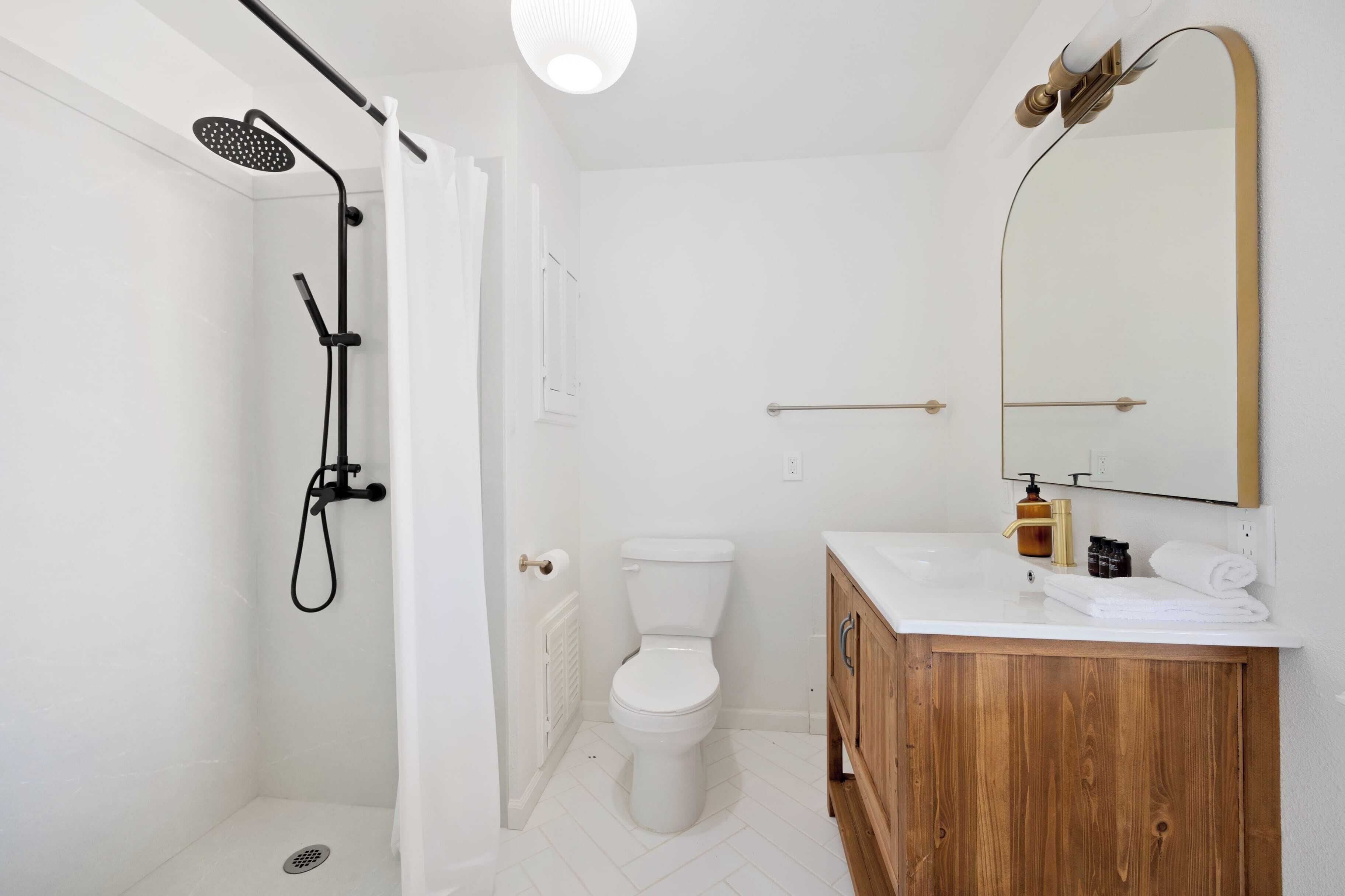 A bathroom with a shower, toilet, vanity, and a large mirror.