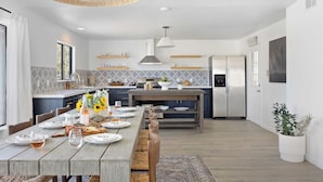 A modern kitchen with a dining area, featuring a large island, built-in appliances, and a hanging light fixture.