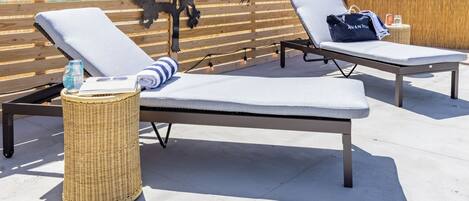 Two lounge chairs with cushions, a wicker basket, and a decorative metal tree.