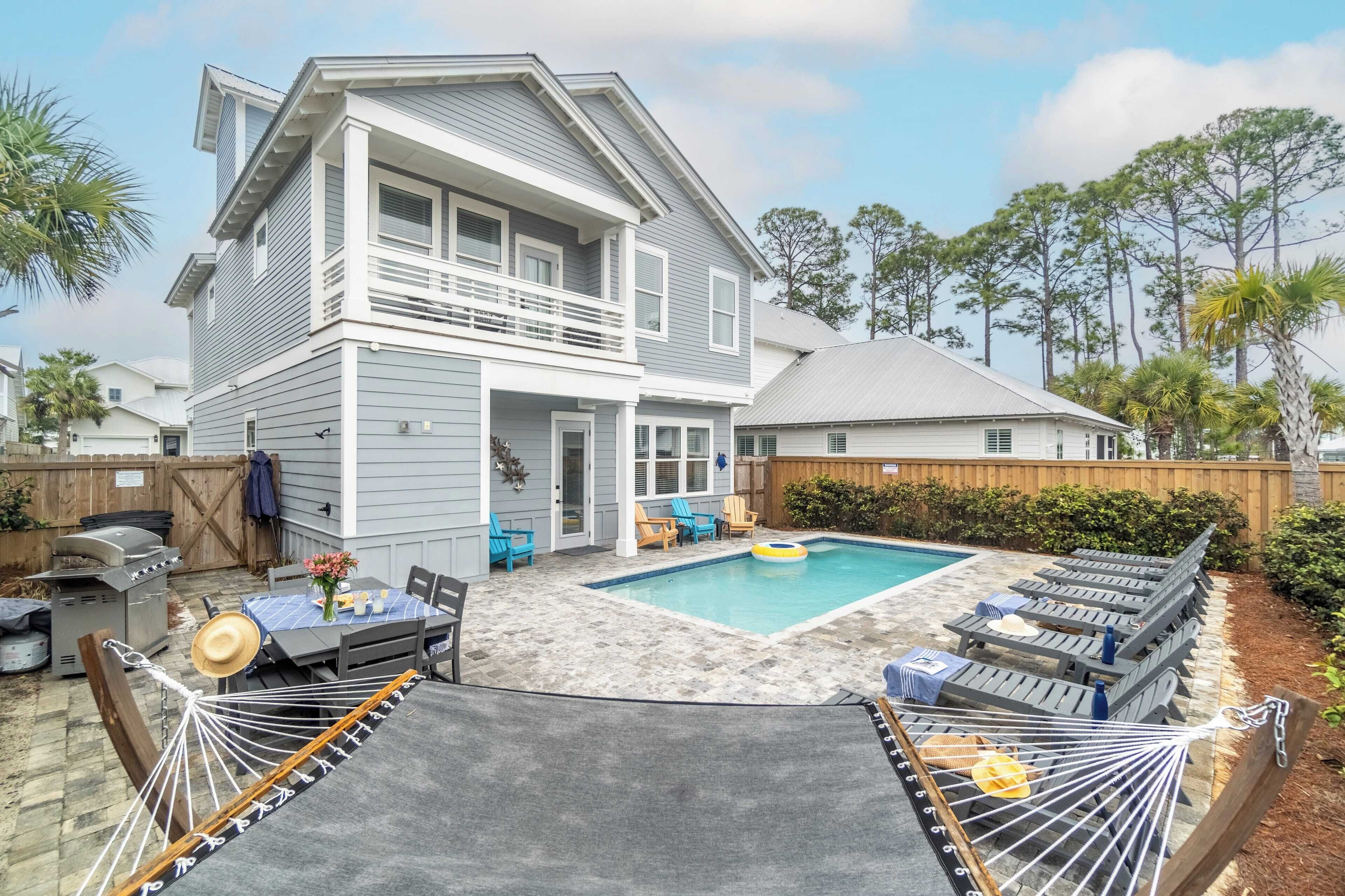 A two-story house with a swimming pool, outdoor seating, and a hammock.