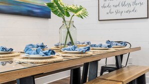 A dining table set with plates, napkins, and a vase with green plants.