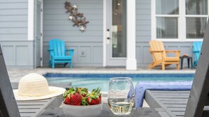 A poolside area with a table, a bowl of strawberries, and a glass of water.
