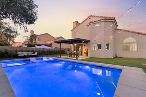A swimming pool with a patio area, a covered seating area, and a house with a tiled roof.