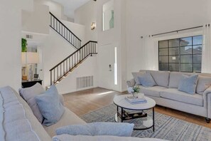 A modern living room with a staircase, a sofa, a coffee table, and a large window.