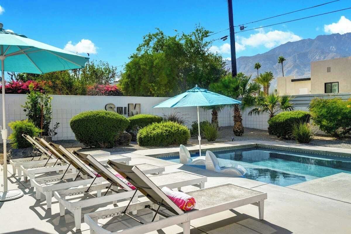 Un espace piscine doté de chaises longues et de parasols, entouré de verdure et avec une chaîne de montagnes en toile de fond.