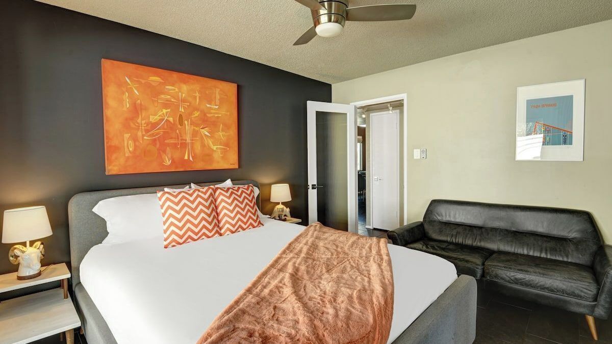 Une chambre d’hôtel avec un lit, un canapé en cuir noir, un ventilateur de plafond et des œuvres d’art accrochées aux murs.