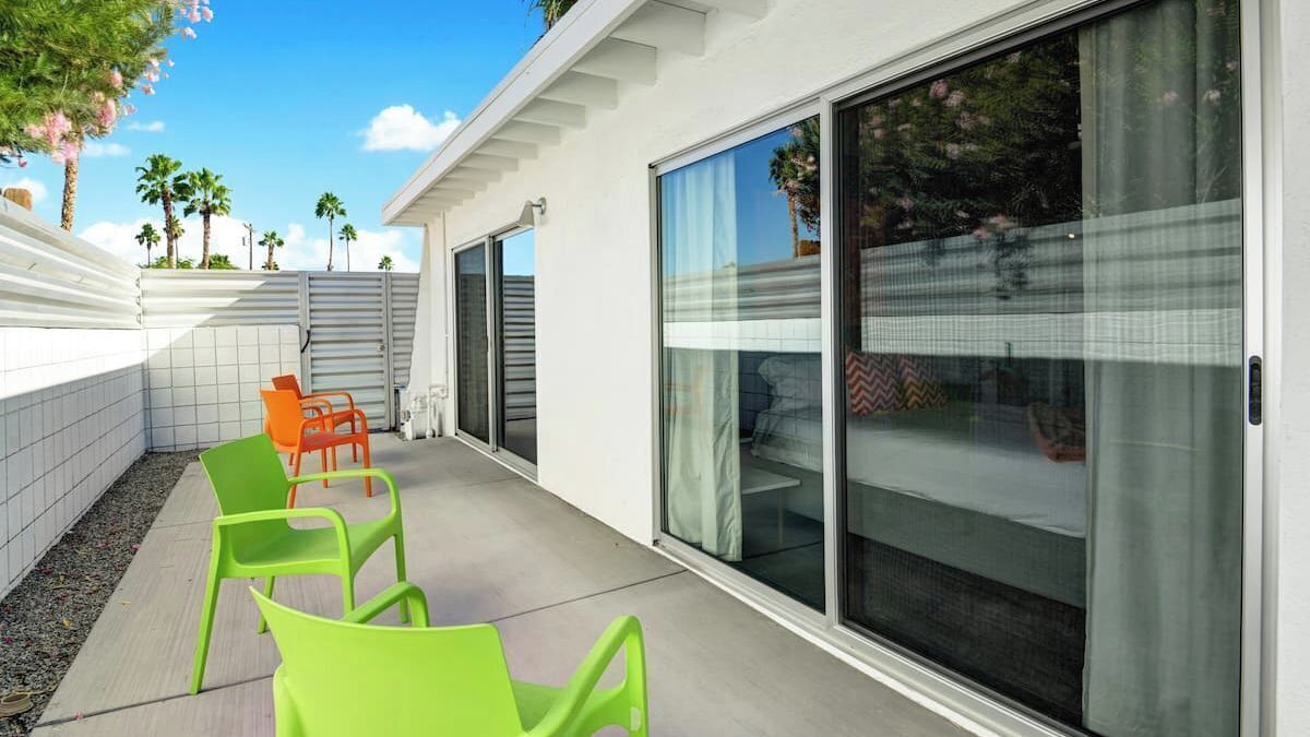Une terrasse extérieure moderne, dotée de portes-fenêtres coulissantes, d’un sol carrelé et de deux chaises vertes.