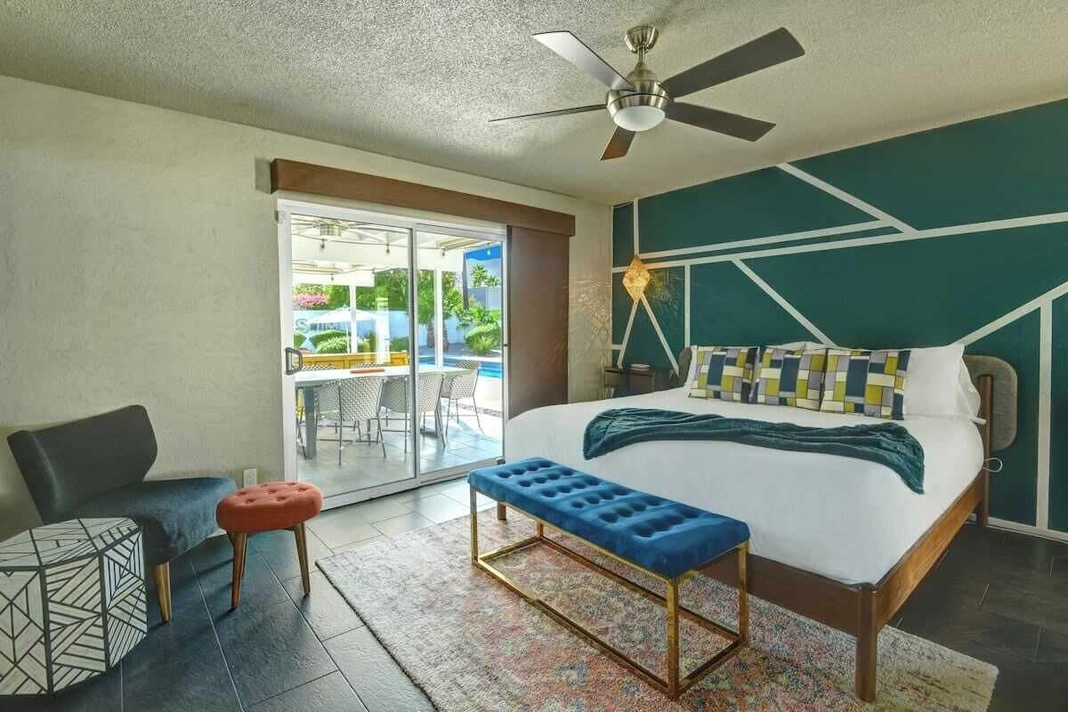 A modern hotel room with a bed, a bench, a chair, and a ceiling fan.