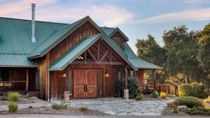 A rustic wooden building with a green metal roof, a large wooden door, and a stone pathway leading to a porch. - Dolcetto by Avantstay Wine Country Mansion, Minutes From Vineyards (Paso Robles)