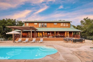 Una casa grande con piscina, mobiliario de exterior y un patio cubierto.